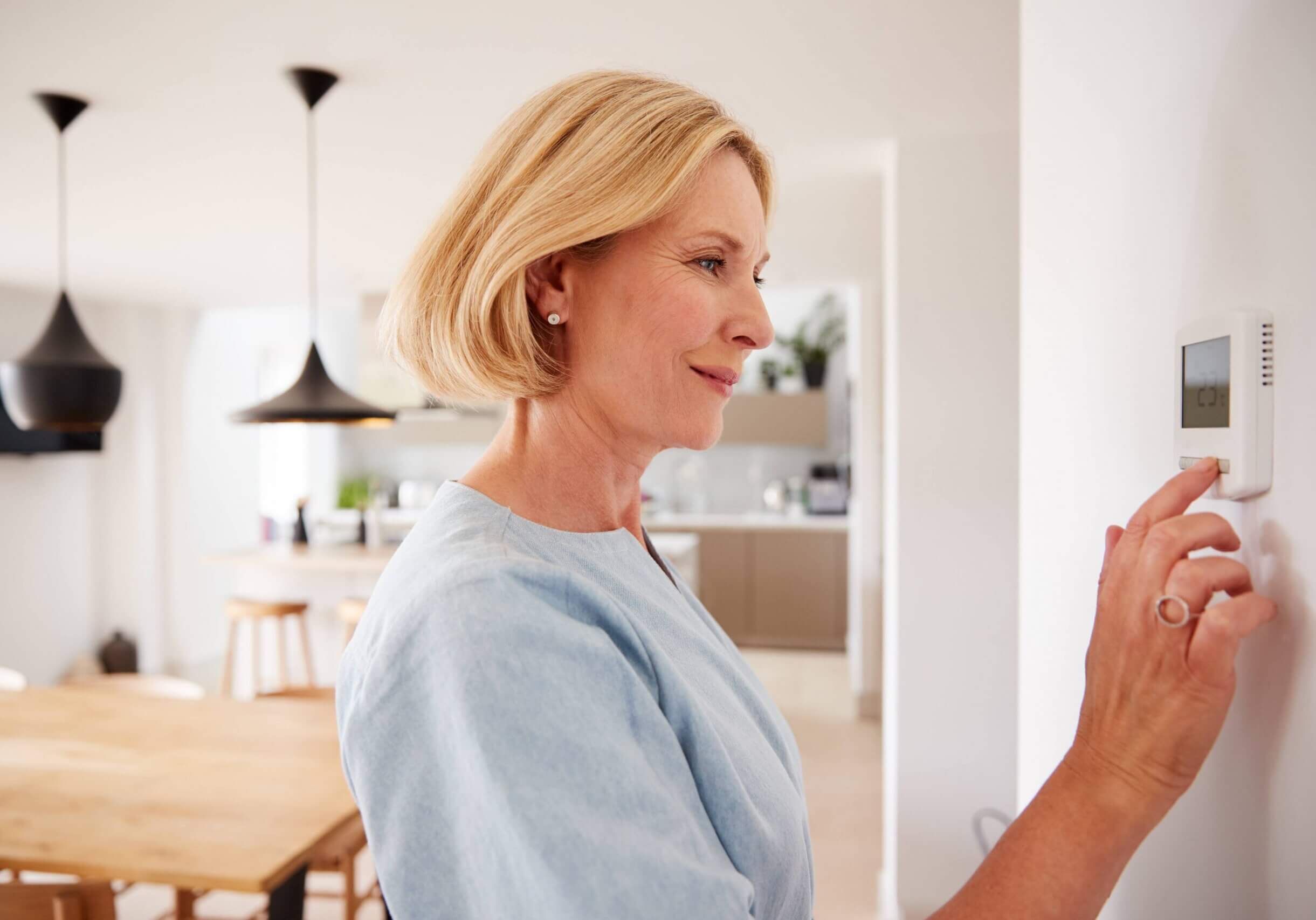 Close Up Of Mature Woman Adjusting Central Heating Temperature At Home On Thermostat